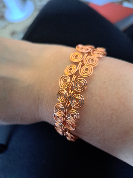 A copper bracelet made up of connected spirals.